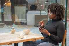 年轻的非洲美国女人坐着咖啡馆杯热咖啡媒体