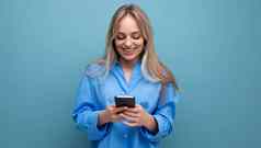 快乐的迷人的金发女郎女人聊天智能手机应用程序蓝色的明亮的背景