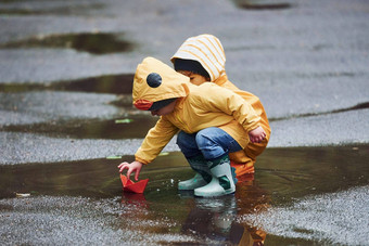 孩子们黄色的<strong>防水</strong>斗篷靴子玩手工制作的纸船在户外雨