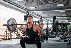 提升杠铃年轻的运动型强大的男人。黑色的穿锻炼一天健身房