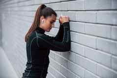 年轻的运动型女孩黑色的运动服装在户外灰色的墙