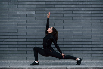 年轻的运动型女孩黑色的运动服装在户外瑜伽练习灰色的墙
