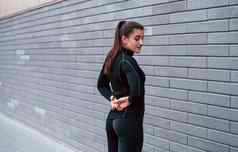 年轻的运动型女孩黑色的运动服装站在户外灰色的墙