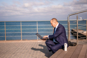 自信中间年龄商人工作远程在线打字移动PC键盘坐着海滩日落工作远程假期运行在线业务距离