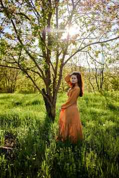可爱的女人站自然明亮的长橙色衣服照亮回来日落射线太阳持有裙子手整理了一下头发