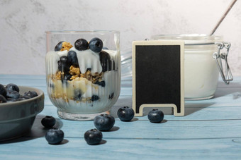 早....格兰诺拉麦片早餐自制的希腊酸奶蓝莓眼镜蓝色的木背景复制空间空黑板上健康的饮食脆脆的格兰诺拉麦片酸奶坚果蓝莓