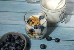 早....格兰诺拉麦片早餐自制的希腊酸奶蓝莓眼镜蓝色的木背景健康的饮食脆脆的格兰诺拉麦片酸奶坚果蓝莓