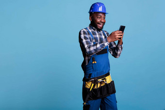 非洲美国构建器接收好新闻文本消息细胞电话乐观承包商穿工作统一的硬他光蓝色的背景工作室拍摄