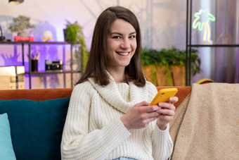 年轻的女人坐着沙发首页智能手机分享消息社会媒体应用程序