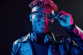时尚的眼镜无线耳机未来主义的霓虹灯照明年轻的非洲美国男人。工作室