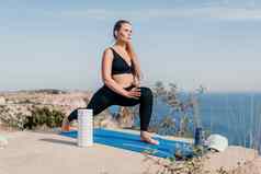 健身女人海户外锻炼瑜伽席辊公园海洋海滩女健身普拉提瑜伽例程概念健康的生活方式快乐适合女人锻炼橡胶乐队公园