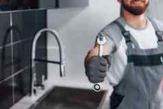 关闭视图年轻的专业水管工灰色统一的持有扳手手厨房