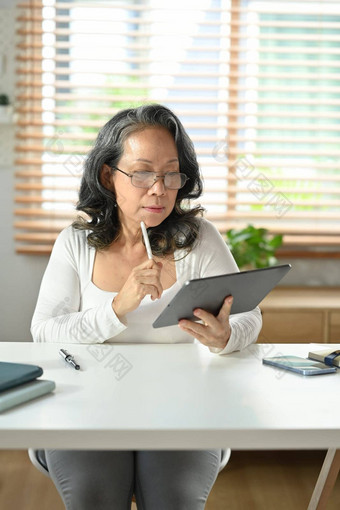 中间岁的亚洲女人坐着舒适的首页办公室浏览无线互联网数字平板电脑上了年纪的技术概念