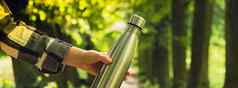 特写镜头认不出来女手持有水瓶横幅可重用的钢热水瓶公园可持续发展的生活方式塑料免费的浪费免费的生活绿色女人喝水公园
