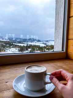 女人持有杯子热咖啡手咖啡馆窗口冬天雪山温暖的白色杯背景冬天森林景观休息放松