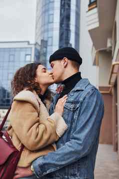 快乐的夫妇休闲温暖的衣服接吻在户外城市业务建筑