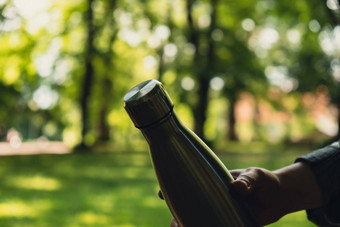 特写镜头认不出来女手持有水瓶可重用的钢热水瓶公园可持续发展的生活方式塑料免费的浪费免费的生活绿色女人喝水公园