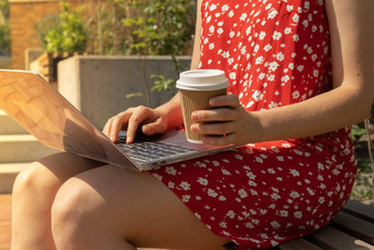 认不出来年轻的女人红色的衣服喝咖啡工艺回收纸杯移动PC自由职业者的的地方工作研究工作在线远程业务教育视图网络研讨会电子学习工作站木板凳上模型咖啡打破