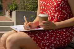 认不出来年轻的女人红色的衣服喝咖啡工艺纸杯写作感激之情杂志木板凳上今天感激的发现杂志反射有创意的写作增长个人发展概念护理幸福精神上的健康