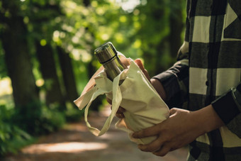特写镜头认不出来女手持有水瓶生态袋可重用的钢热水瓶公园可持续发展的生活方式塑料免费的浪费免费的生活绿色女人喝水公园