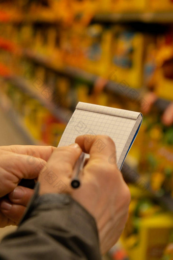 女手持有纸笔记本购物列表模糊货架上背景部分视图女人购物超市概念消费主义关闭女人使笔记购物列表