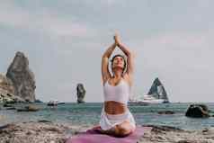 健身女人海快乐中间岁的女人白色运动服装练习早....在户外海滩火山岩石海女健身普拉提瑜伽例程概念健康的生活方式
