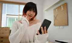 微笑年轻的亚洲女人发短信消息聊天在线移动电话坐着现代首页办公室