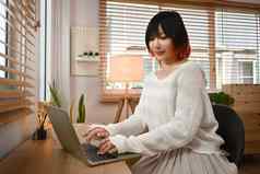 漂亮的年轻的亚洲女人移动PC浏览互联网检查视频社会网络坐着舒适的生活房间