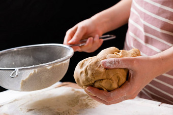 关闭女人初步整理小麦面粉筛混合碗面团准备蛋糕面包店黑色的背景揉面团自制的糕点