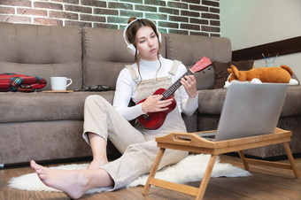 爱好休闲活动检疫在线培训在线类年轻的女人手表视频教训玩吉他坐在舒适的格子吉他