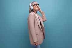 女人祖母时尚的夹克听音乐大耳机明亮的背景复制空间