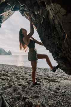 体育女人攀爬岩石年轻的女人苗条的适合身体攀爬火山玄武岩洞穴美丽的海视图运动员女孩火车自然女人克服了困难攀爬路线