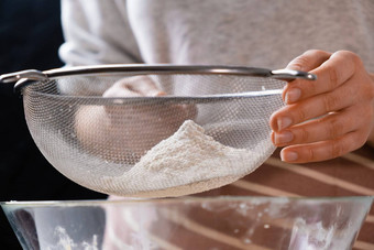 关闭女人初步整理小麦面粉筛混合碗面团准备蛋糕面包店黑色的背景揉面团自制的糕点