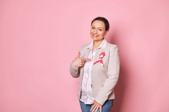 积极的多民族女人站粉红色的背景指出手指粉红色的缎丝带夹克