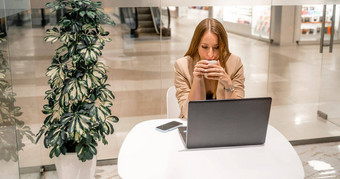 业务女人坐在咖啡馆作品电脑饮料咖啡穿米色夹克棕色（的）前黑色的裤子