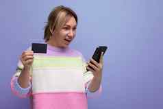 金发碧眼的女孩使购买互联网持有聪明的电话信贷卡模型手紫色的背景