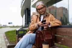 高级成人上了年纪的女人坐在公园街读取消息移动电话一年欧洲女人