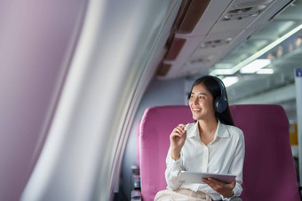 年<strong>轻</strong>的亚洲有吸引力的业务女人乘客坐着业务类<strong>奢</strong>侈品飞机穿无线耳机放松工作平板电脑飞行
