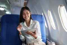 亚洲有吸引力的业务女人乘客坐着业务类奢侈品飞机平板电脑电脑旅行概念