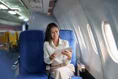 亚洲有吸引力的业务女人乘客坐着业务类奢侈品飞机平板电脑电脑旅行概念