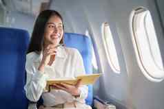 亚洲业务女人乘客坐着业务类奢侈品飞机工作笔记本书旅行概念