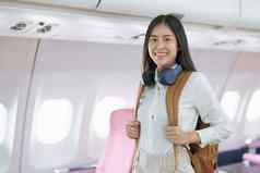 年轻的亚洲有吸引力的女人旅行飞机乘客穿耳机把手行李储物柜座位飞机