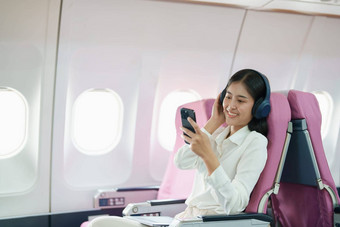 年<strong>轻</strong>的亚洲有吸引力的业务女人乘客坐着业务类<strong>奢</strong>侈品飞机穿无线耳机聪明的电话移动放松飞行
