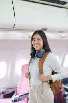 年轻的亚洲有吸引力的女人旅行飞机乘客穿耳机把手行李储物柜座位飞机