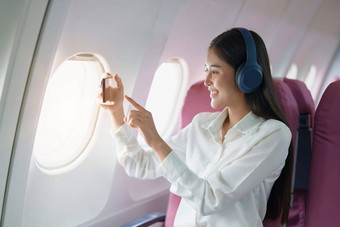 年<strong>轻</strong>的亚洲有吸引力的业务女人乘客坐着业务类<strong>奢</strong>侈品飞机穿无线耳机聪明的电话移动放松飞行