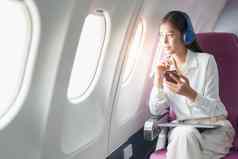 年轻的亚洲有吸引力的业务女人乘客坐着业务类奢侈品飞机穿无线耳机聪明的电话移动放松飞行