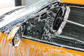 黄色的车一边窗口洗<strong>服务</strong>洗车冲叶子中风洗发水泡沫玻璃