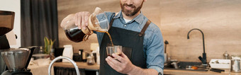 微笑咖啡师时尚的胡子穿围裙倒过滤器咖啡玻璃