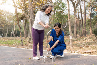 护士帮助上了年纪的女人调整沃克护士持有手上了年纪的女人走公园设施