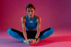 活跃的健身女人穿运动服装坐着地板上伸展运动腿工作室背景